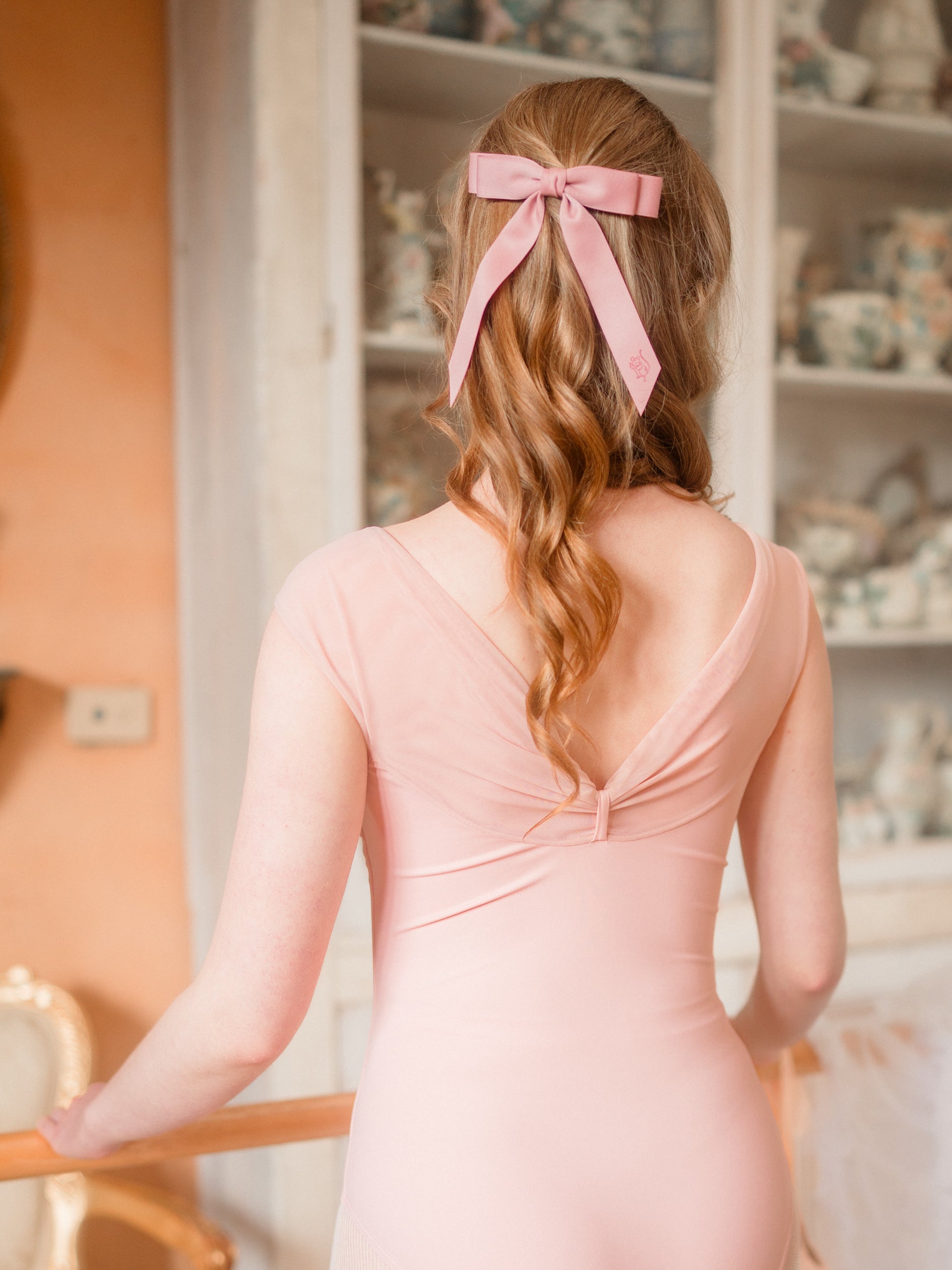 Ballerina in a ballet pose in a room with decorative items and furniture. Mesh and buttery stretch fabric leotard, Australian small batch dancewear.